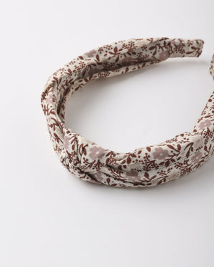A stylish and comfortable Girls’ Knotted Headband by Rylee & Cru, featuring a twisted knot design with a brown floral pattern on a cream background, is displayed on a white surface.