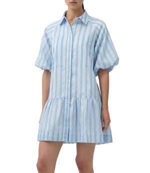 A woman wears the Simkhai Crissy Stripe Dress, a light blue and white satin mini shirtdress featuring puffed short sleeves and a collar.