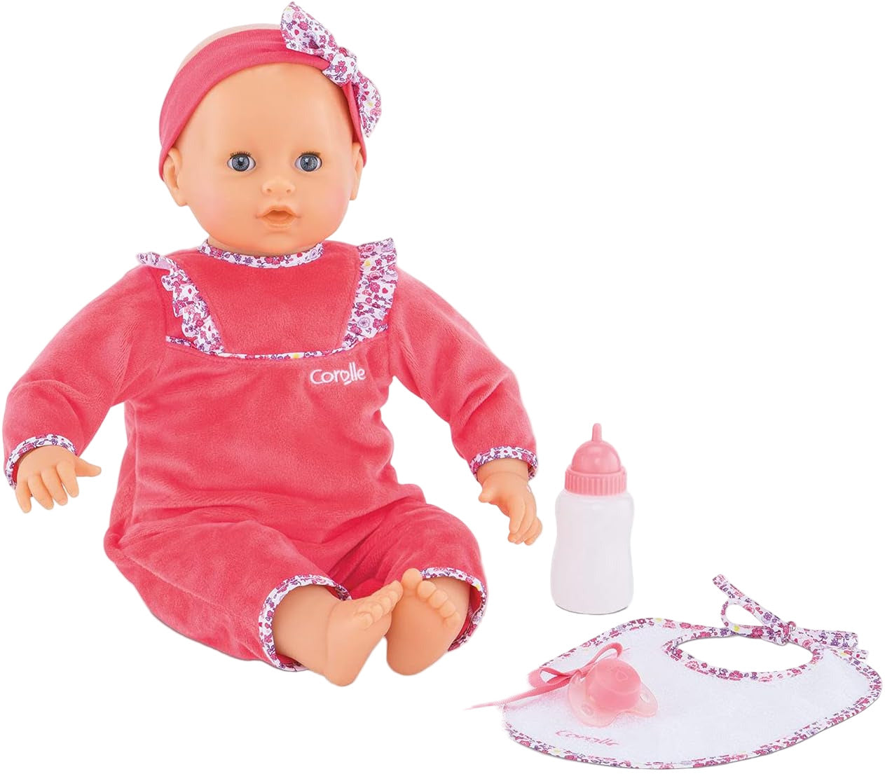The Corolle Lila Chérie 17" baby doll, dressed in pink with a headband and made of soft-touch vinyl, sits beside a white bottle, pacifier, and matching bib.