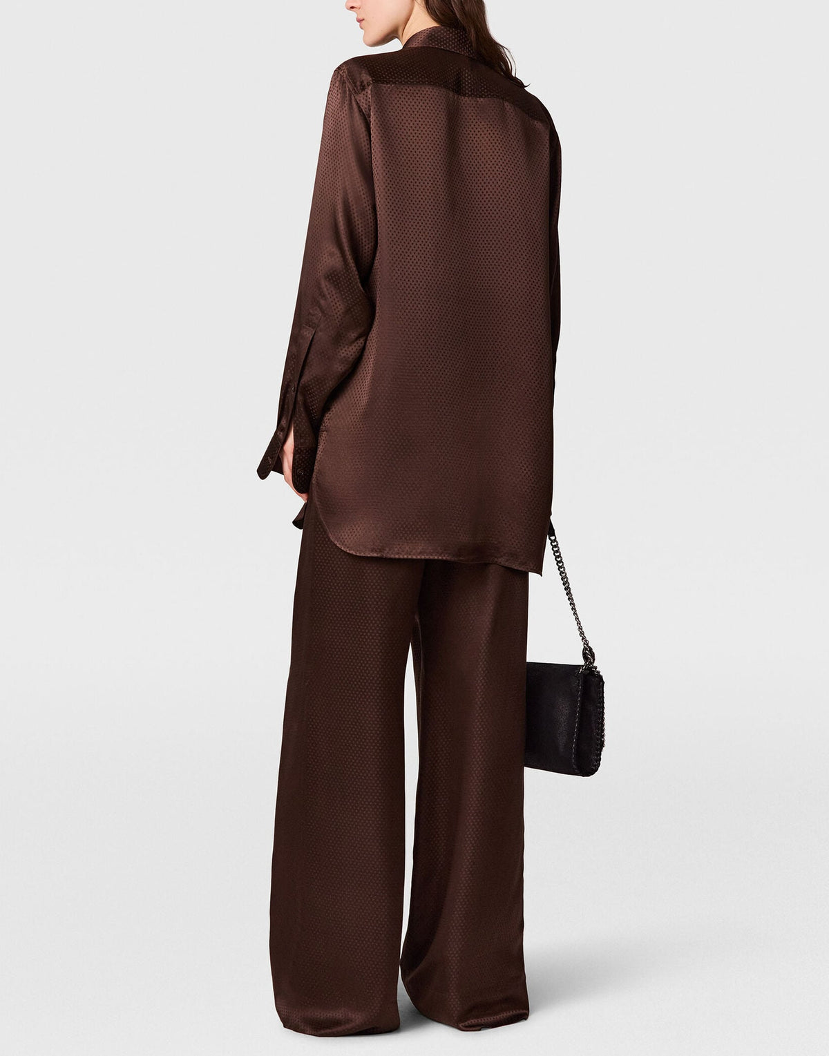 A person wearing a Stella McCartney Star Silk Jacquard Shirt with wide-leg dark brown trousers, carrying a small black shoulder bag.