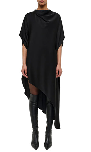 Wearing the Simkhai Sadia Cape Mini Dress—a loose-fitting, asymmetrical black mini with short sleeves, draped high neckline, and asymmetric hem—paired with over-the-knee black boots for a chic, modern glamour vibe.