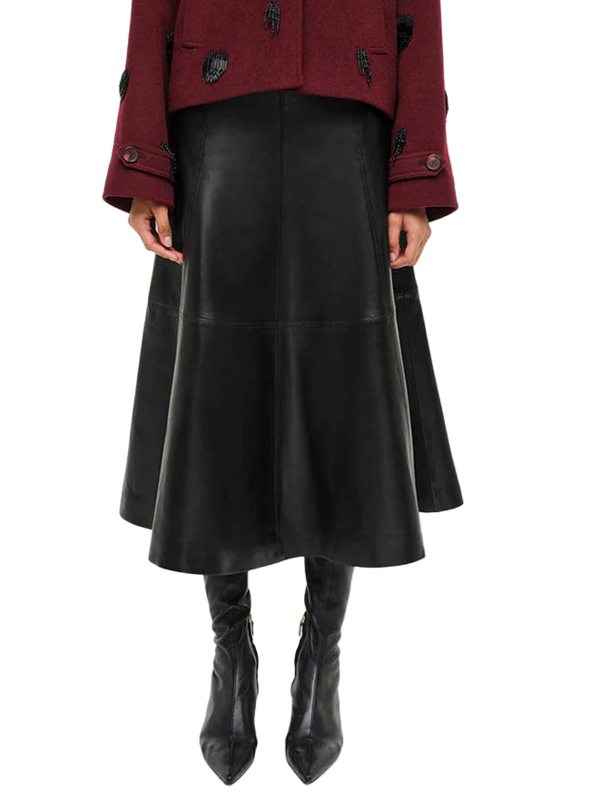 Shown from shoulders to feet, a person in Simkhai's Ryma Leather Midi Skirt, styled with a burgundy jacket and black heeled boots, captures elevated dressing with a sleek silhouette.