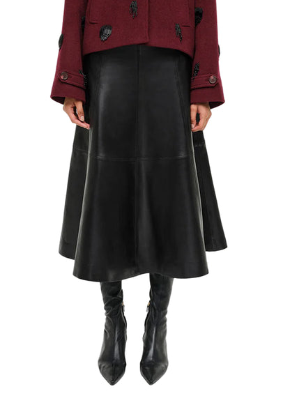 Shown from shoulders to feet, a person in Simkhai's Ryma Leather Midi Skirt, styled with a burgundy jacket and black heeled boots, captures elevated dressing with a sleek silhouette.