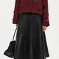 A person wearing a maroon jacket, black knee-high boots, a black handbag, and the Simkhai Ryma Leather Midi Skirt stands against a white background, showcasing a sleek silhouette ideal for elevated style.