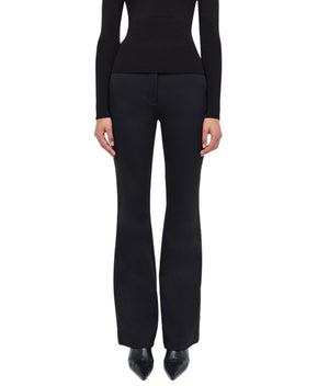 A person stands facing forward against a white background, embodying refined minimalism in the Simkhai Kenna Trouser paired with a fitted black long-sleeve top.