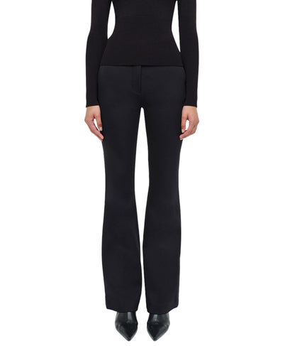 A person stands facing forward against a white background, embodying refined minimalism in the Simkhai Kenna Trouser paired with a fitted black long-sleeve top.