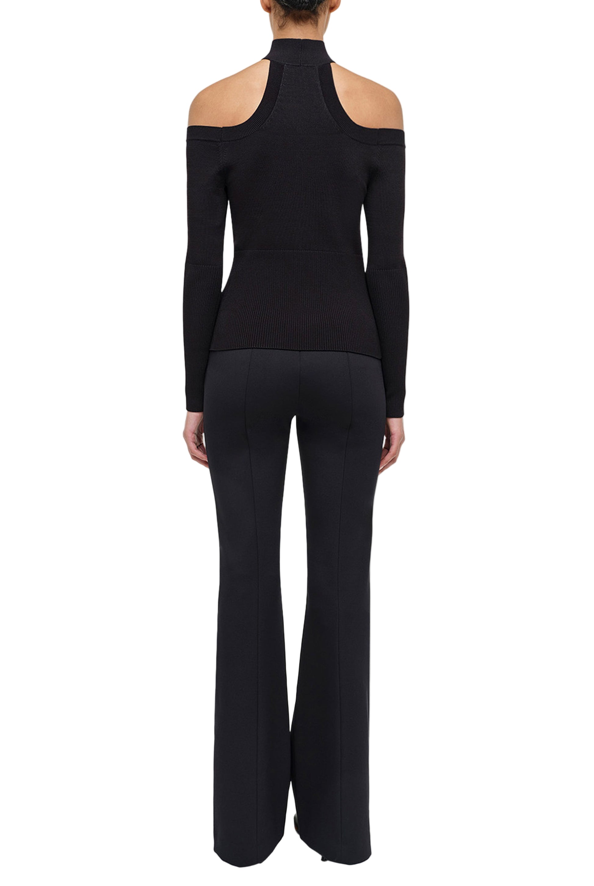 A person is shown from the back wearing a black, long-sleeve cold-shoulder top and Simkhai's Kenna Trouser in flared double twill, capturing refined minimalism against a white background.