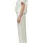 Woman in side profile wears the Simkhai Louisa Camp Shirt in white with floral embroidery, matching wide-leg pants, and white platform sandals.