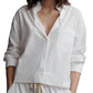 A woman in a TWP Day After Top, a relaxed fit white cotton poplin button-up shirt with a chest pocket, paired with drawstring pants.