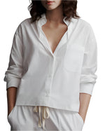 A woman in a TWP Day After Top, a relaxed fit white cotton poplin button-up shirt with a chest pocket, paired with drawstring pants.