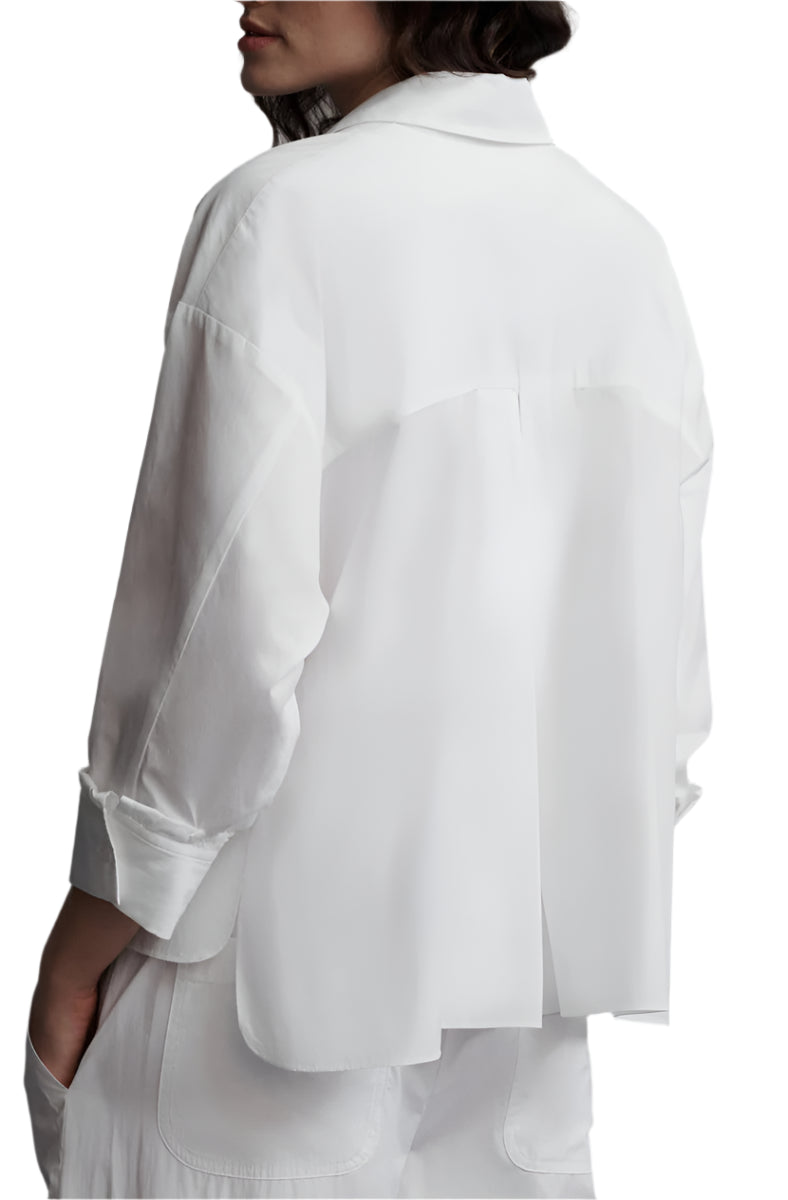 Against a plain background, a person is seen from behind wearing the TWP Day After Top, a relaxed fit cotton poplin shirt, paired with white pants, exuding effortless style.