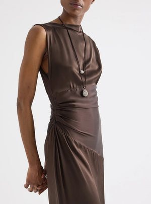 Model wears TWP's On The Side Dress, a brown sleeveless silk charmeuse style with side ruching, paired with two long necklaces, posed against a plain light background.