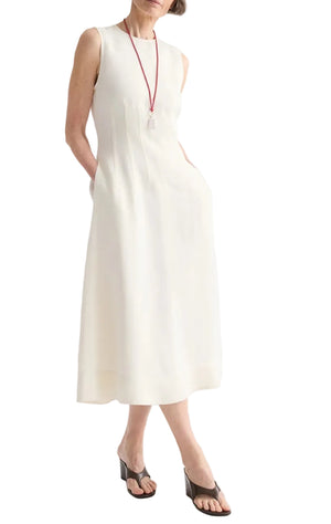 A person wearing the TWP Crew Neck Coated Viscose Linen Dress with side pockets, paired with black heeled sandals and a long red necklace.