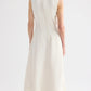 A person with short gray hair faces away, wearing the TWP Crew Neck Coated Viscose Linen Dress, a sleeveless cream A-line style, paired with heeled sandals.