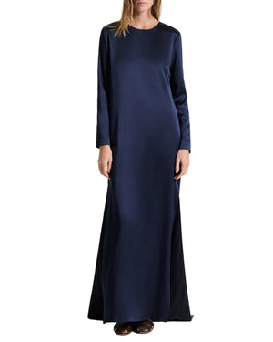 A person wearing the dark navy Nightfall Dress by TWP, a long-sleeved, floor-length style with side slits.