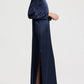 A person wears a long-sleeved, navy blue floor-length TWP Nightfall Dress with a side slit and dark sandals.