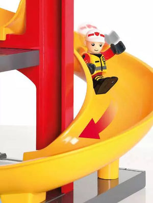 A Brio World toy fireman is riding down a yellow slide.