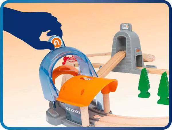 A hand interacts with the BRIO World Action Tunnel Deluxe Set, featuring Smart Tech Sound technology, an Action Tunnel, and trees from Brio for enhanced railway fun.