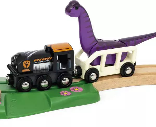 The BRIO Dinosaur Adventure Set by Brio features a toy train with an engine and carriage holding a purple dinosaur, running on a wooden track adorned with flower decorations on the green platform area.