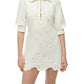 A woman wears the Simkhai Freya Linen Dress—an ivory mini with embroidery, long sleeves, a collared neckline, partial button front, and scalloped hem. This chic linen piece is perfect as a sunny-day cover-up.