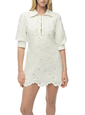 A woman wears the Simkhai Freya Linen Dress—an ivory mini with embroidery, long sleeves, a collared neckline, partial button front, and scalloped hem. This chic linen piece is perfect as a sunny-day cover-up.