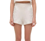 A person wearing Simkhai's Sammie Short—high-waisted white linen shorts with delicate soutache embroidery—and a matching cropped top, arms relaxed at their sides.