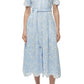 A woman wears the Simkhai Audria Belted Midi Dress in light blue with short sleeves and a waist tie, styled with white heeled sandals for a chic look.