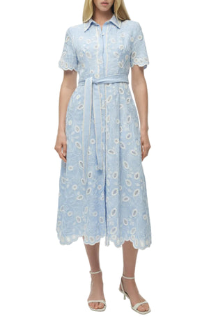 A woman wears the Simkhai Audria Belted Midi Dress in light blue with short sleeves and a waist tie, styled with white heeled sandals for a chic look.