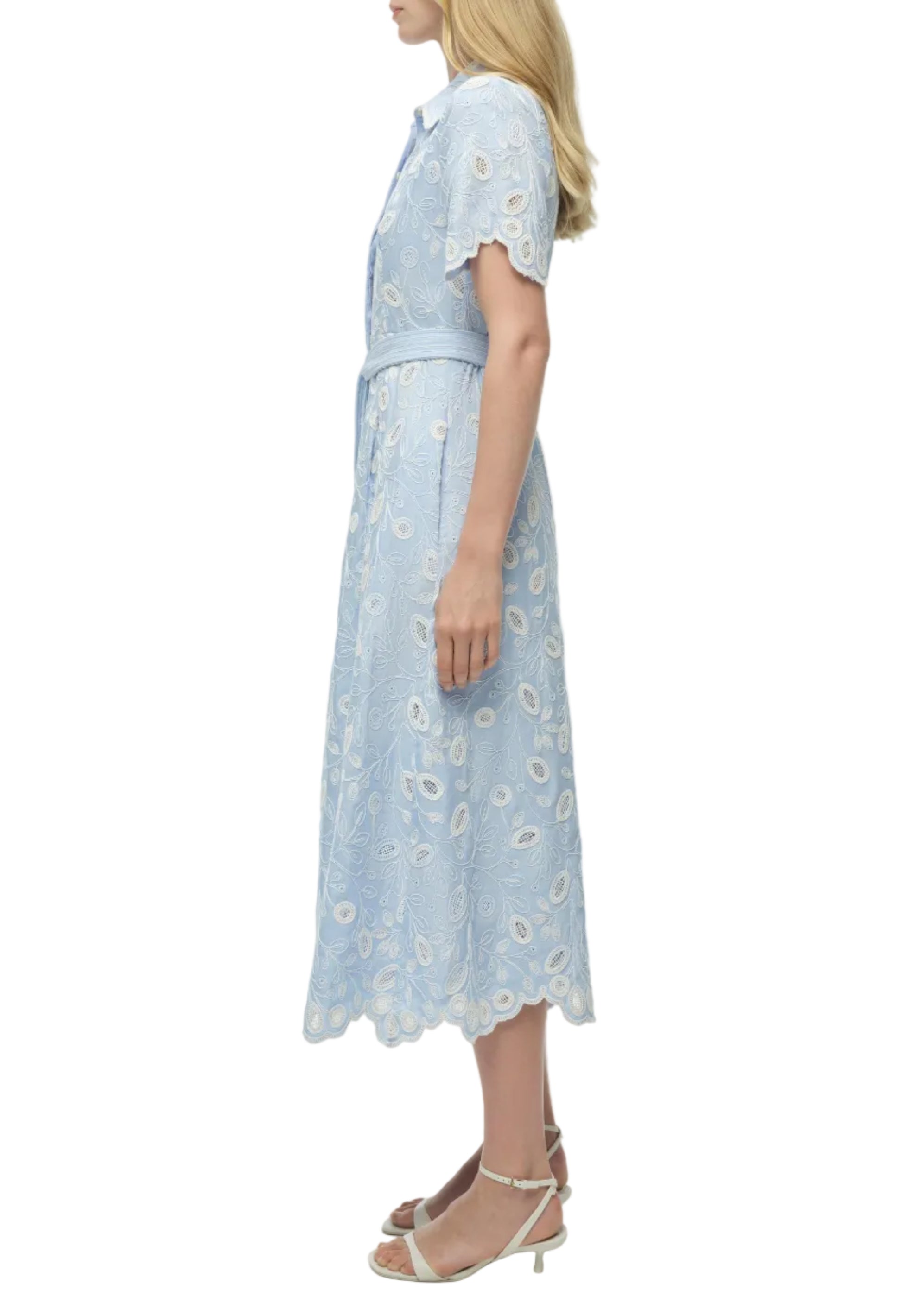 Woman in profile wears the Simkhai Audria Belted Midi Dress in light blue lace with scalloped edges, paired with white heeled sandals.