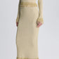 A Simkhai Zeni Midi Skirt, styled as a long-sleeved, high-neck metallic bouclé midi dress with pearl-trimmed fringe at the waist, cuffs, and hem, paired with thin-strapped white heels.