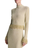 Simkhai Tali Pearl Fringe Top in a long-sleeved, high-neck metallic bouclé knit with a pearl fringe hem and cuffs.
