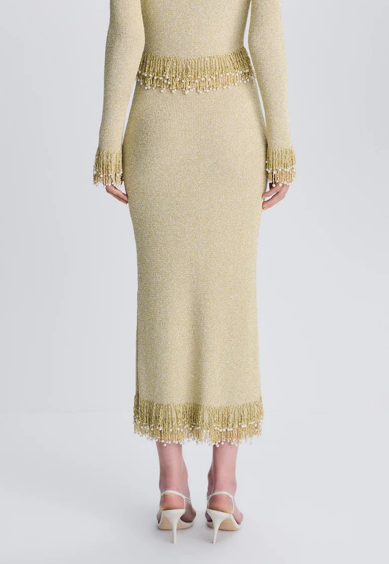 Back view of the Simkhai Zeni Midi Skirt in gold metallic bouclé, featuring pearl-adorned fringe trim at the waist and hem.