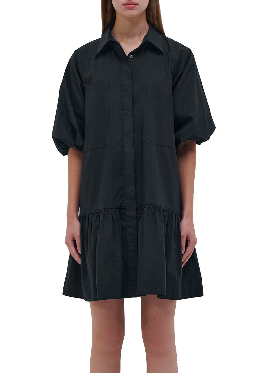 Person wearing a black Simkhai Crissy Dress with ballooned short sleeves and a button-up front. The dress, which falls above the knees, features a loose, ruffled hem for a casual mini dress look.