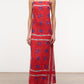 A person wears the Laura Linen Maxi Dress by Staud—a red sleeveless summer dress with blue star patterns and white stripes—paired with black flip-flops, standing against a plain background.