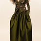 A person wears a dark lime Bernadette Oscar skirt, a matching embroidered cardigan, and black heeled pumps.