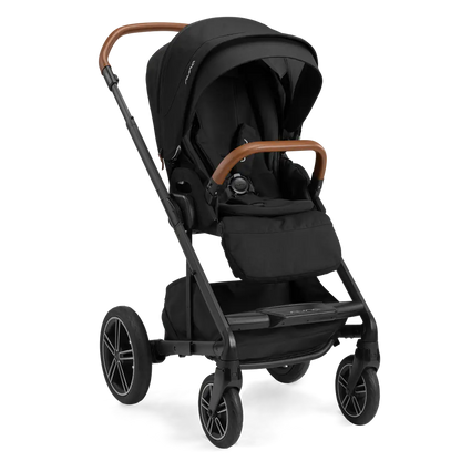 The Nuna MIXX Next Stroller in black, showcasing stylish brown handles and large wheels, is pictured from a three-quarter angle. Its compact folding design and MagneTech Secure Snap™ provide both elegance and practicality for every trip.