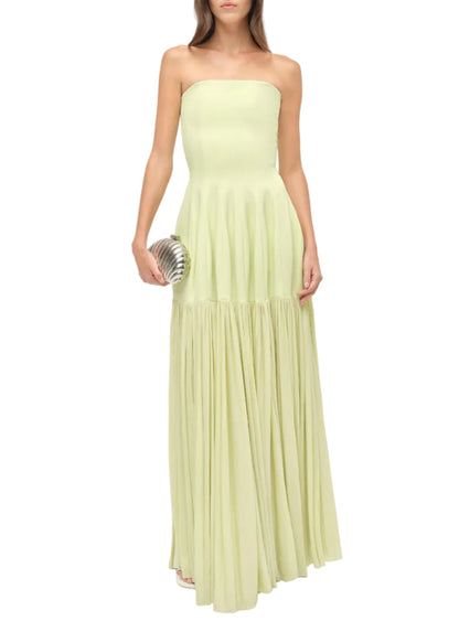 A woman in the Simkhai Sandrine Dress, featuring a strapless paneled bodice and elongated silhouette, holds a silver clutch by her side.