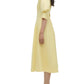 A woman in profile wears the Simkhai Jazz Pintuck Midi Dress, a light yellow cotton A-line style with elbow-length sleeves, paired with white strappy heeled sandals.