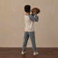 A child, dressed in the Rylee & Cru Boys’ Long Sleeve Raglan Tee pajamas, stands on a wooden floor holding a football and facing away from the camera against a beige wall, enjoying the breathable comfort of soft fabrics.