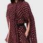 A person wears the Stella McCartney Tie-Neck Polka Dot Silk Dress—a maroon dress adorned with white polka dots, featuring a tie-neck detail and loose, flowing sleeves. The midi silhouette is cinched at the waist with a black belt, creating an effortlessly stylish look.