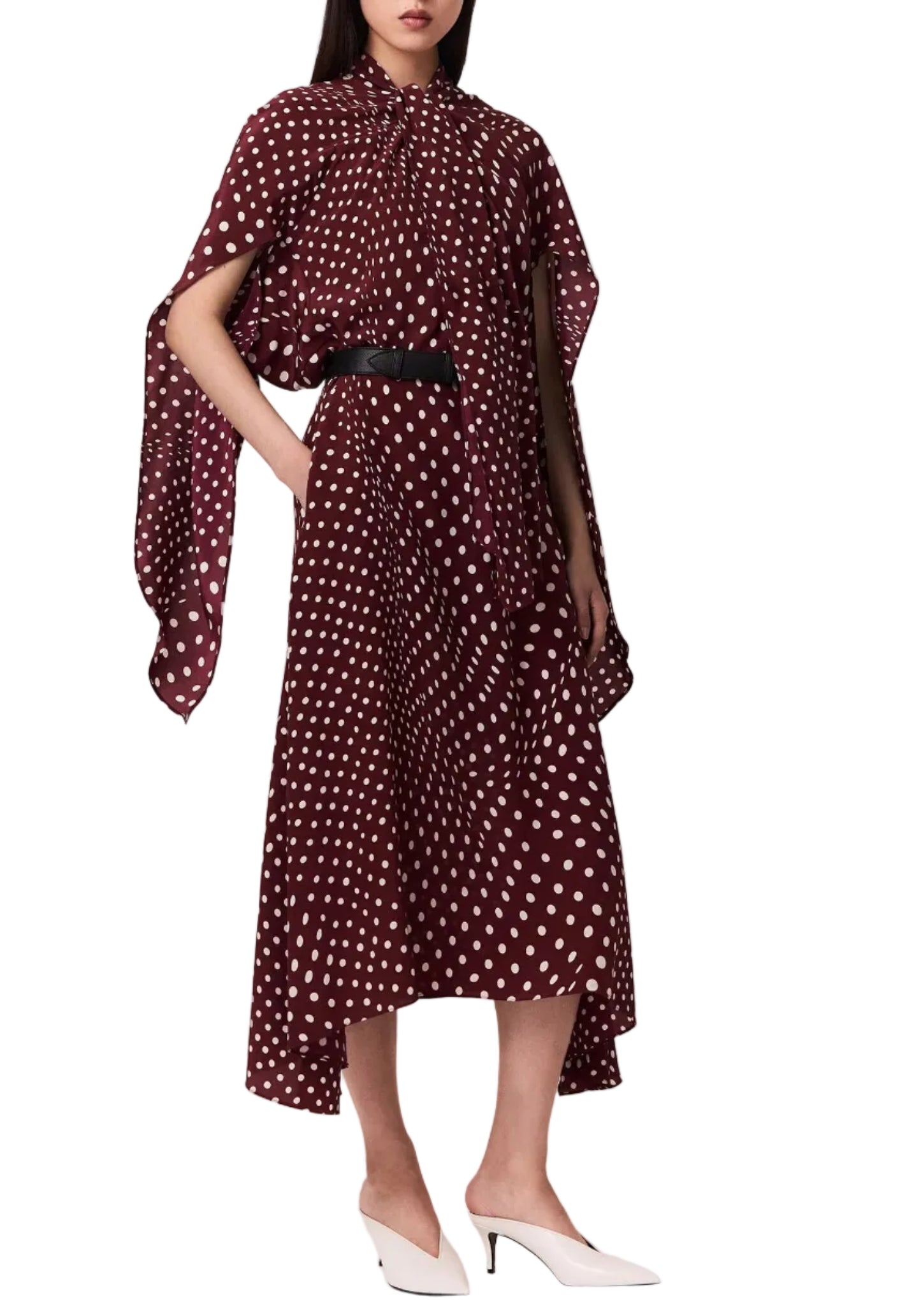 A woman models the Stella McCartney Tie-Neck Polka Dot Silk Dress, a maroon, ankle-length piece with a classic midi silhouette and tie-neck detail, styled with a black belt, white heels, and a draped cape accent, set against a white background.