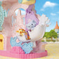 Calico Critters Baby Dream Amusement Park features toy giraffe and elephant figures riding in a white, swan-shaped carnival car, set against a pastel playset backdrop with blue skies, decorative buildings, and a colorful Ferris wheel.