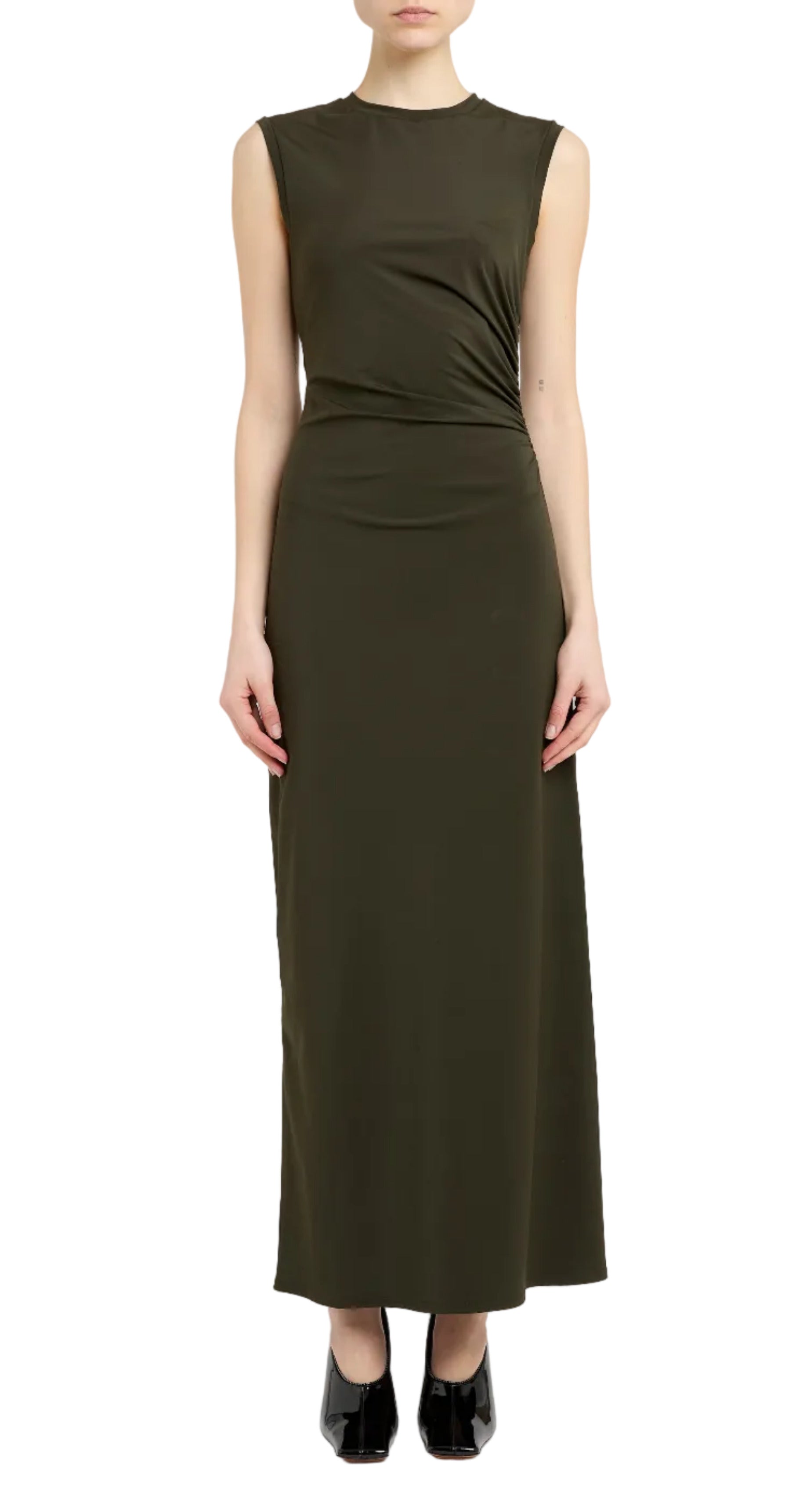 A woman models the Stella McCartney Fluid Jersey Long Dress, a sleeveless dark olive green maxi with a fitted waist, paired with black shoes and set against a white background.