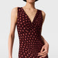 A woman wearing the Stella McCartney Polka Dot Mesh V-Neck Midi Dress, featuring a sleeveless design with maroon polka dots, pink accents, and a V-neckline, stands against a plain background.