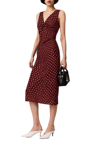 A person wearing the Stella McCartney Polka Dot Mesh V-Neck Midi Dress, a sleeveless maroon dress with white dots, styled with a black handbag and white low-heeled shoes.