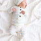 A newborn baby dressed in the Lou Lou & Company Baby Conrad Top & Bottoms, featuring a white design with dotted stripes and a matching hat, lies on a soft white blanket facing left. This cozy set is crafted from silky-soft fabric and includes built-in footies to keep your little one snug and comfortable.