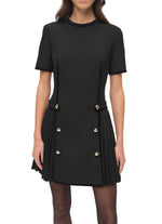 A woman wearing the Simkhai Doria Mini Dress, a fitted black velvet style featuring gilded buttons and pleated side panels.