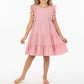 A young girl stands barefoot against a white background, wearing the Mer Girls’ Sophie Tassel Dress—a sleeveless, knee-length dress crafted from lightweight cotton with ruffle details and a tiered skirt.