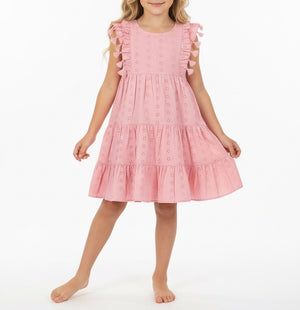 A young girl stands barefoot against a white background, wearing the Mer Girls’ Sophie Tassel Dress—a sleeveless, knee-length dress crafted from lightweight cotton with ruffle details and a tiered skirt.