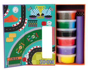 Open box reveals Floss and Rock’s Cars Clay & Play set, featuring vibrant play dough containers stacked beside a racing-themed play mat with track, finish line, and “zoom” graphics—ideal for creative fun or pairing with an air-dry clay sculpting kit.